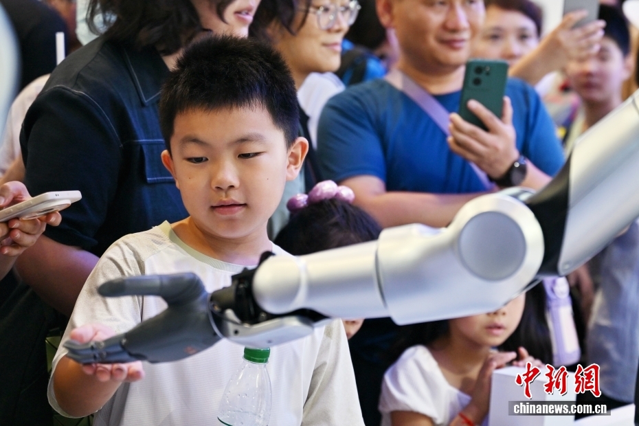 中新社记者 王紫儒 摄 8月10日正值周末，世界机器人大会人气旺。2025世界机器人大会于8月8日至12日在北京亦庄举行，主题为“让机器人更智慧，让具身体更智能”。图为小观众触摸机器人。