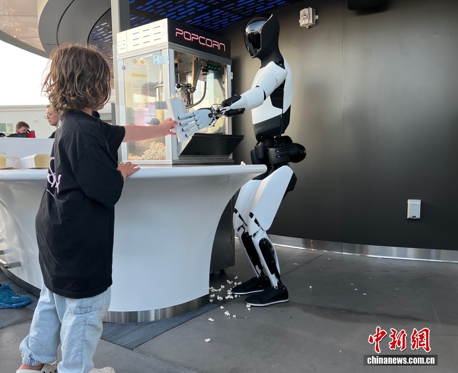 当地时间7月21日下午，美国人工智能巨头特斯拉公司的首家超级充电站餐厅在洛杉矶正式向公众开放，无特斯拉车辆也可访问。图为特斯拉首家超级充电站餐厅内，特斯拉人形机器人“Optimus”给小朋友派发爆米花。 中新社记者 张朔 摄